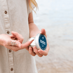 women's finger with a blob of sunscreen on it from a tin